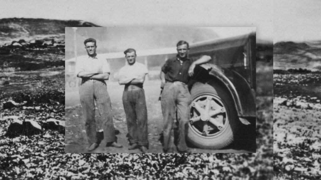 Foto in bianco e nero, 3 uomini accanto a un furgone, sullo sfondo un deserto dell'Africa